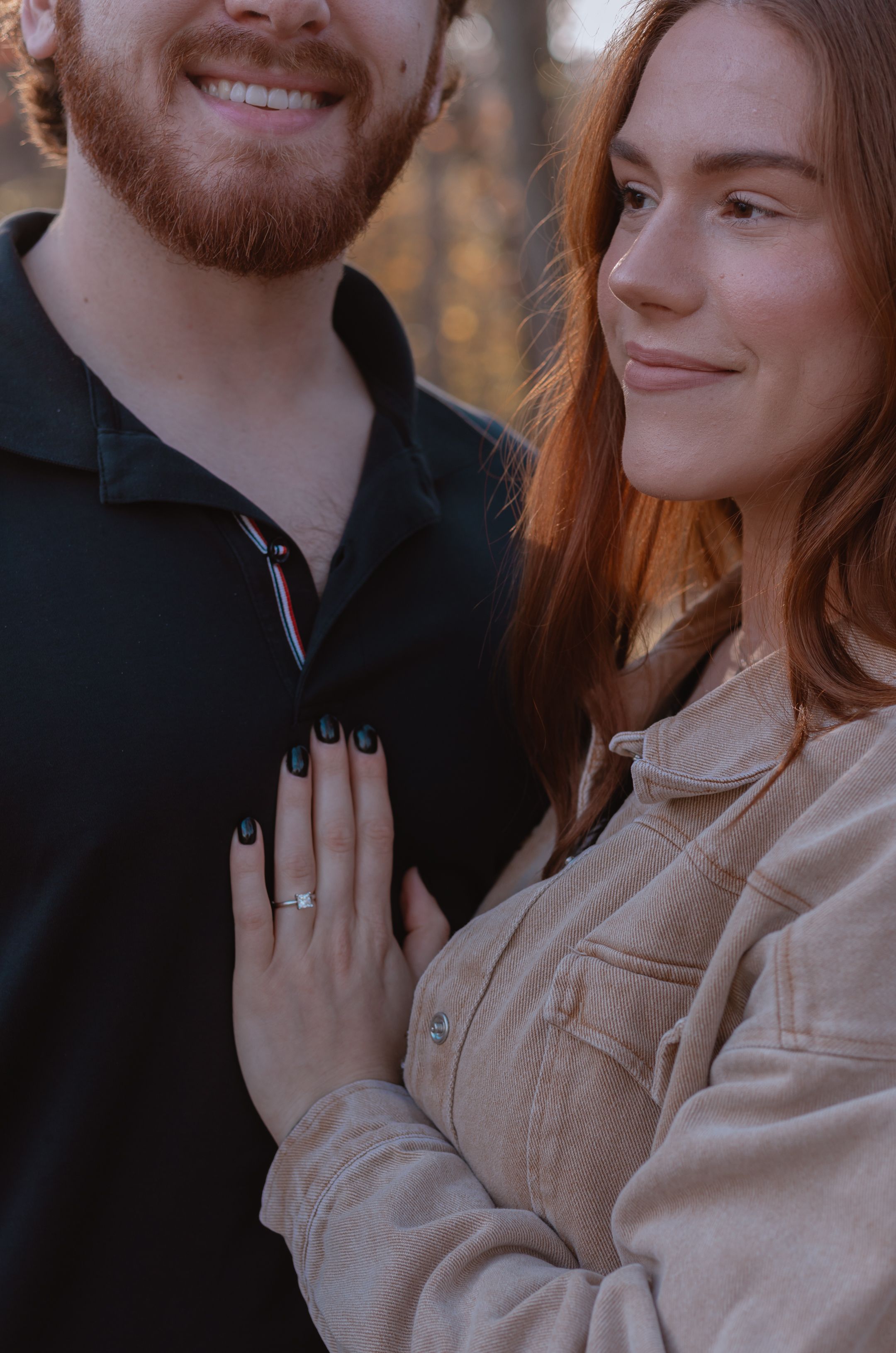 A romantic couple smiles together outdoors during an autumn engagement photoshoot.