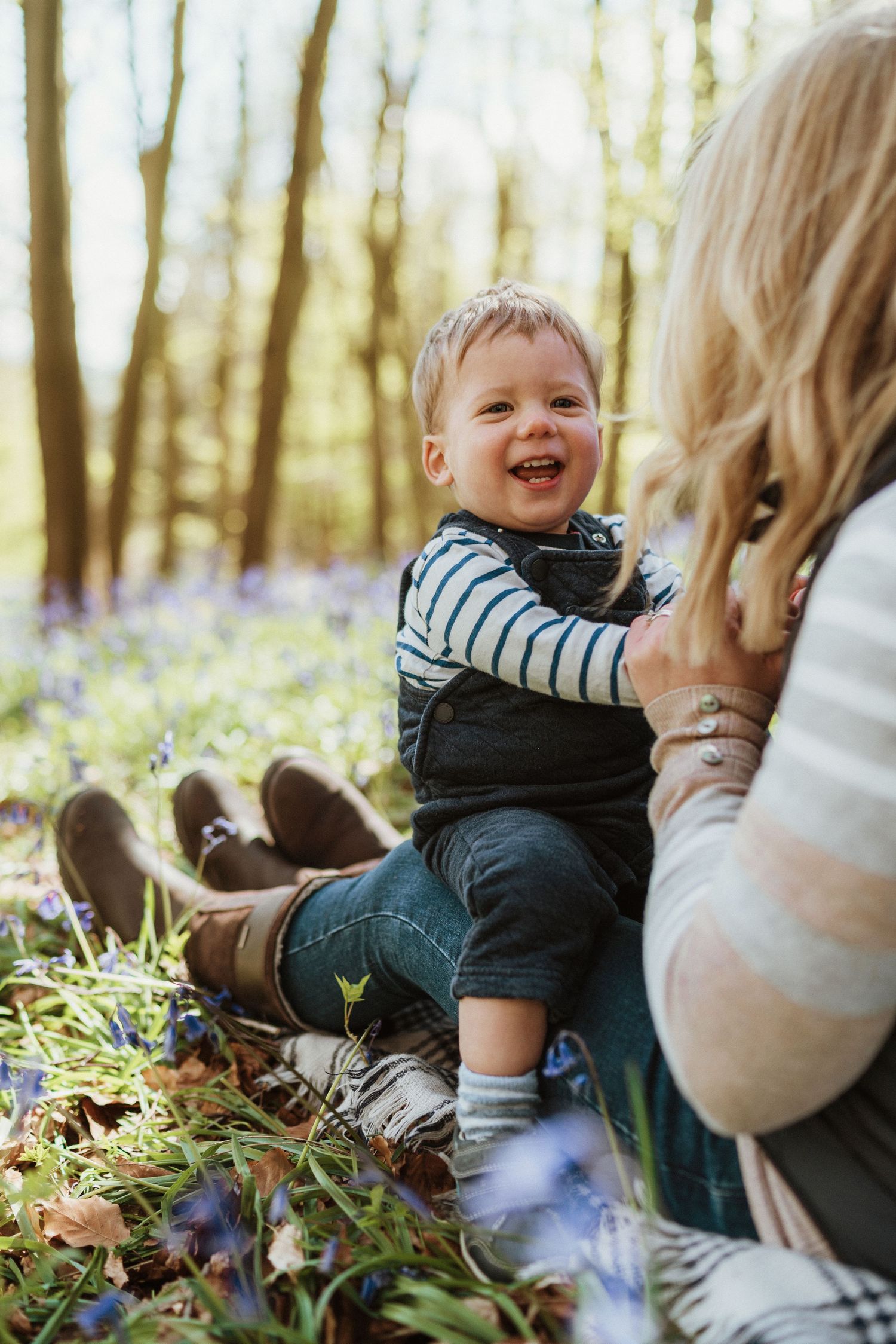 A joyful moment captured in a bluebell forest as a small child laughs while sitting on the ground.