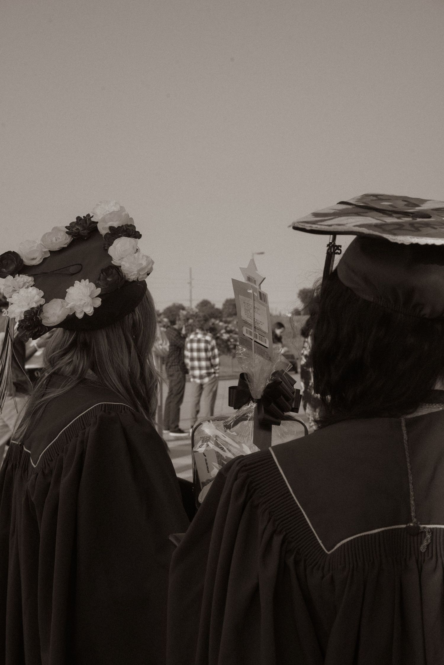 Black and white photo showing graduates in caps and gowns standing in a row during commencement ceremony.