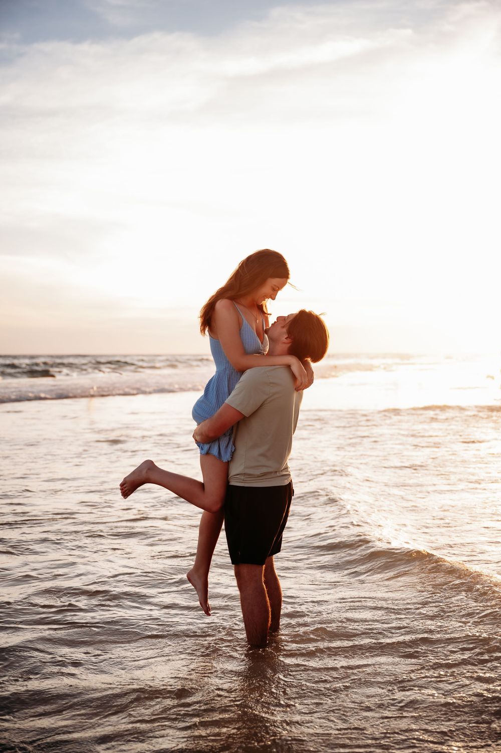 A couple embraces in shallow ocean waves during sunset at the beach.