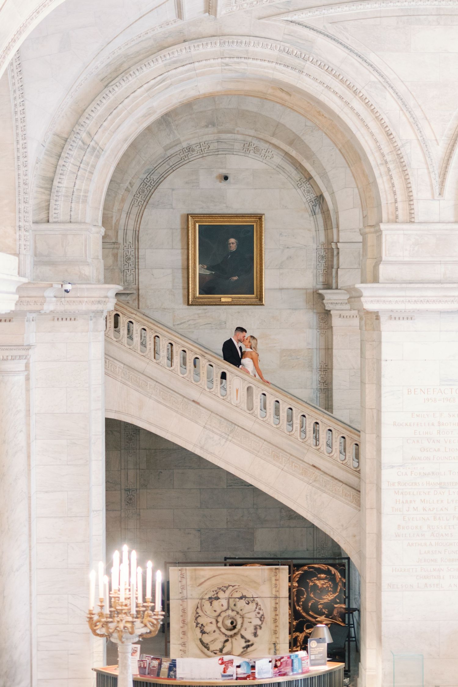 Elegant wedding couple embracing on a grand staircase inside a stunning neoclassical building with arched ceilings.
