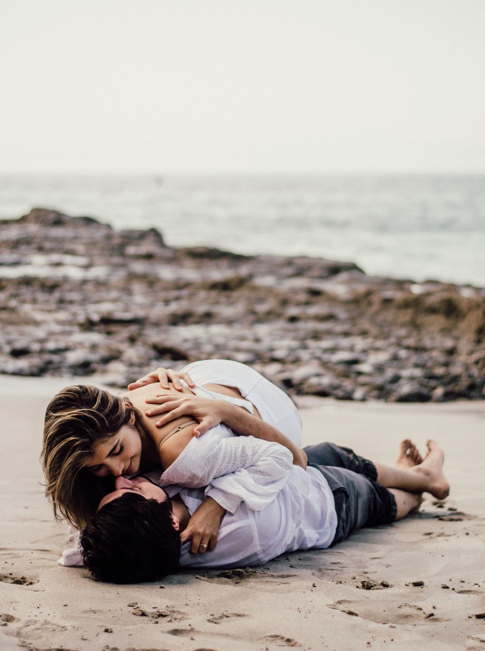 Intimate moment shared on a rocky beach with waves in the background.