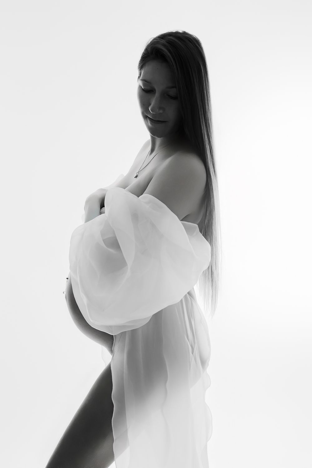Artistic black and white maternity photo series showing silhouette of pregnant woman in flowing white fabric.