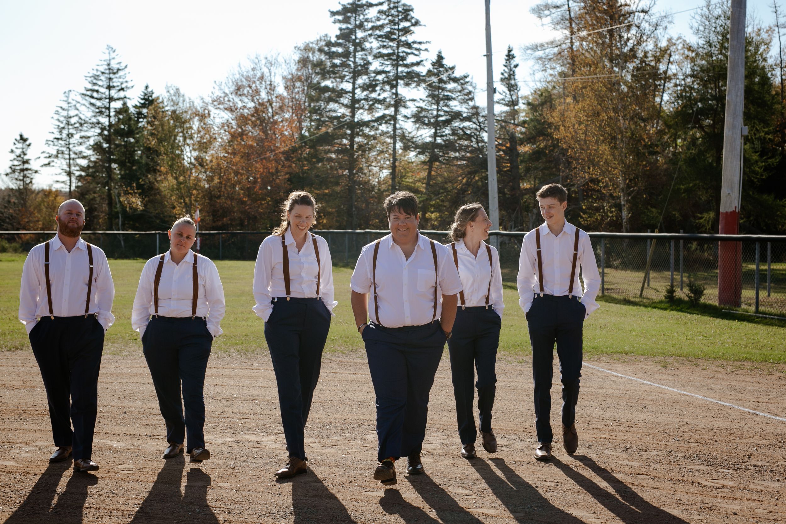 Bride and bridesmaids / groomsmen walking in baseball field. Photography by Samantha Bateman. Nova Scotia wedding photographer.