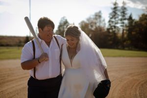 Bride and bride walking in baseball field. Photography by Samantha Bateman. Nova Scotia wedding photographer.