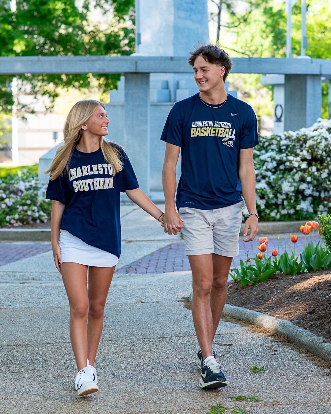 High school senior couple holding hands while wearing future college T-shirts during an outdoor senior portrait session.
