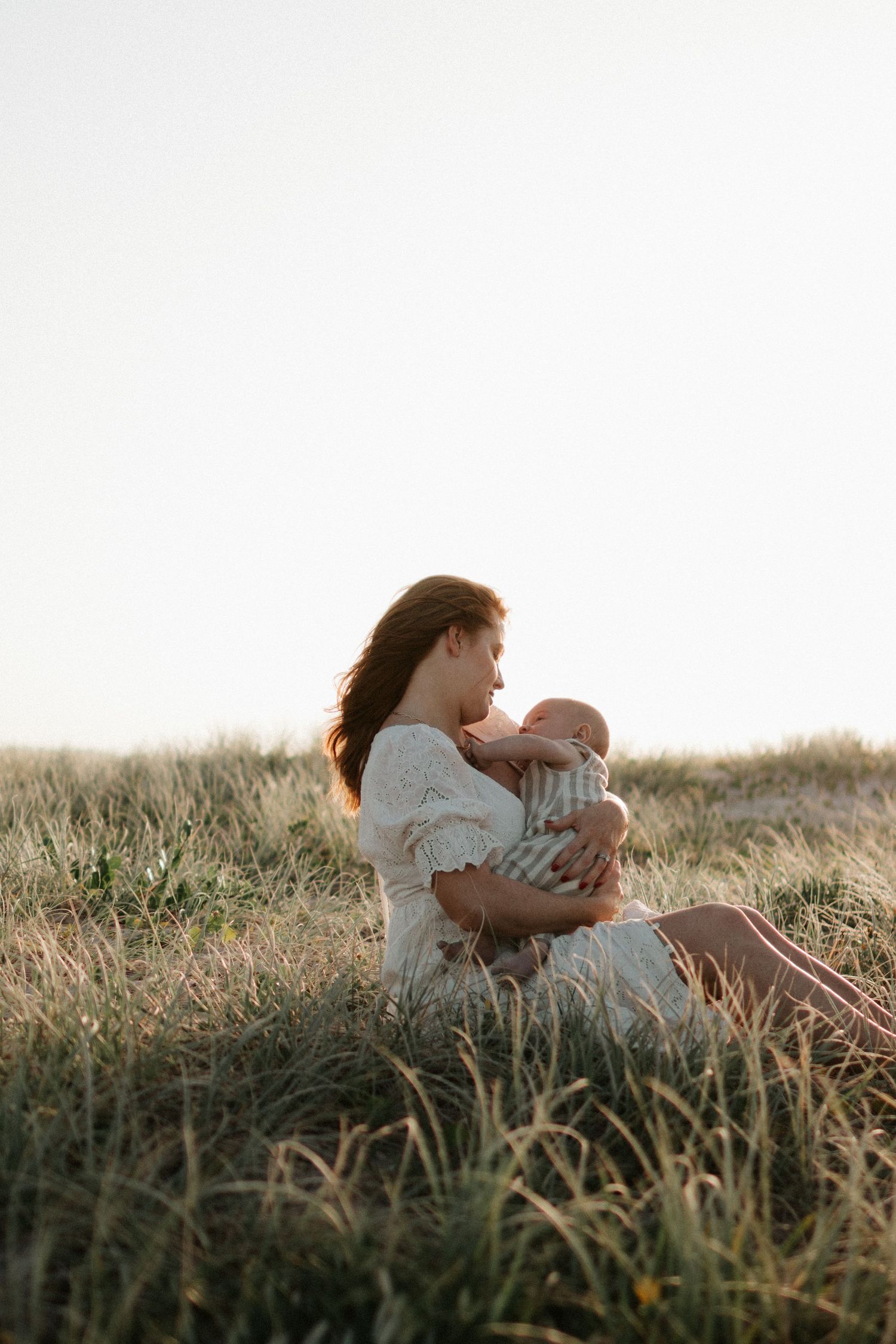 Mother and baby sharing tender moment in sunlit field of tall grass.
