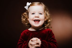 Smiling toddler in red velvet dress with bow poses for portrait.