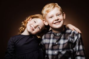 Two young siblings lean together for heartwarming studio portrait.