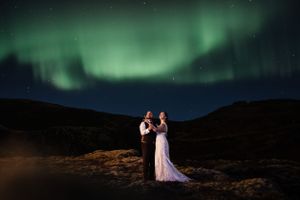 A couple embracing under the stunning green aurora borealis in a dark mountainous landscape.
