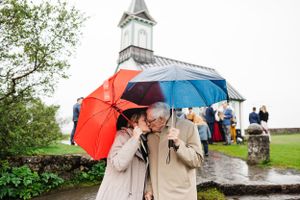 A couple shares an intimate moment under colorful umbrellas outside a white chapel.