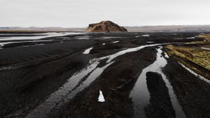 Winding waterways cut through black volcanic sand with a rocky hill rising from Iceland's dramatic landscape.