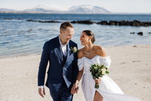 A romantic beachside wedding photo with mountains in the background on a sunny day.