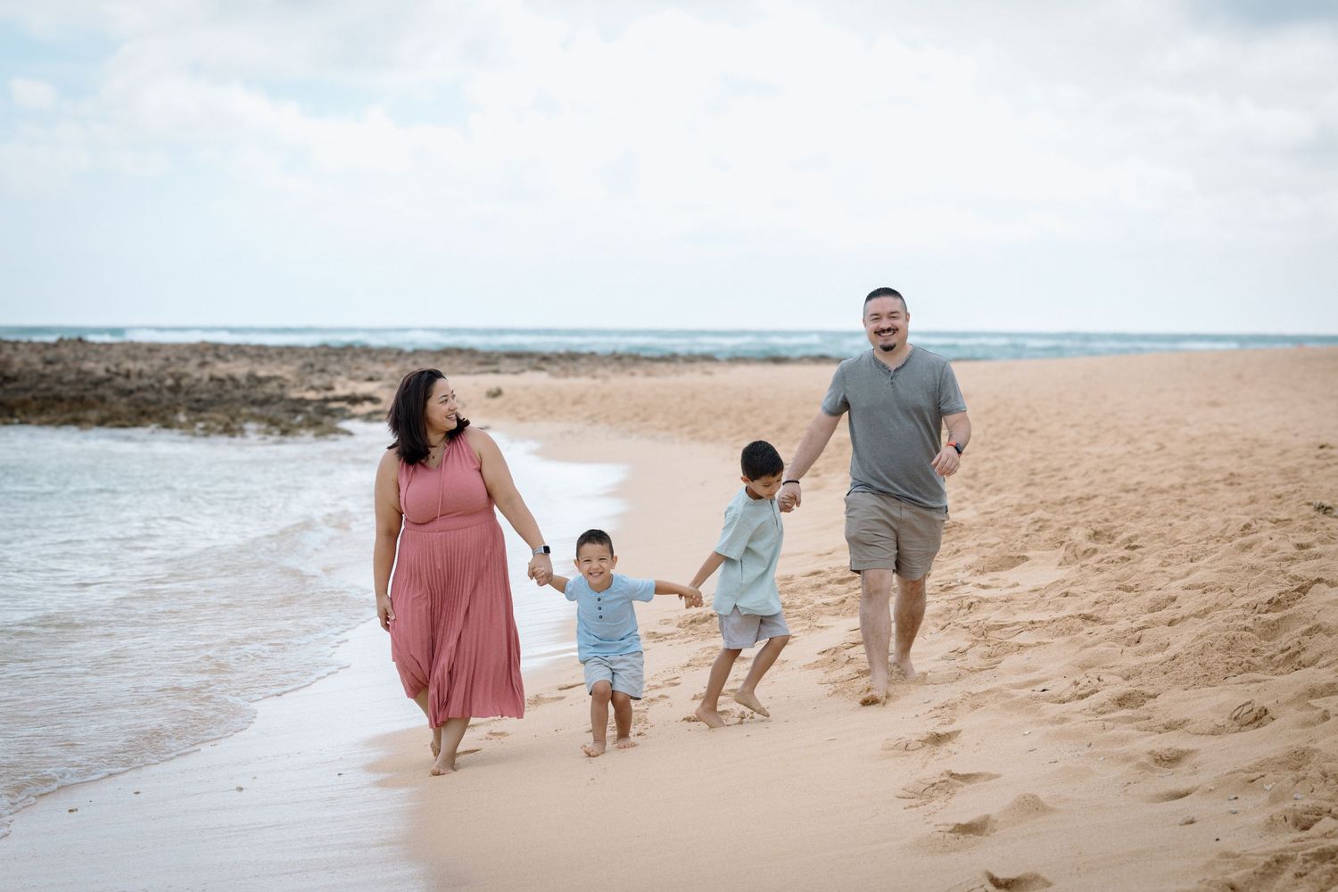 A family holds hands while walking together on a scenic beach.