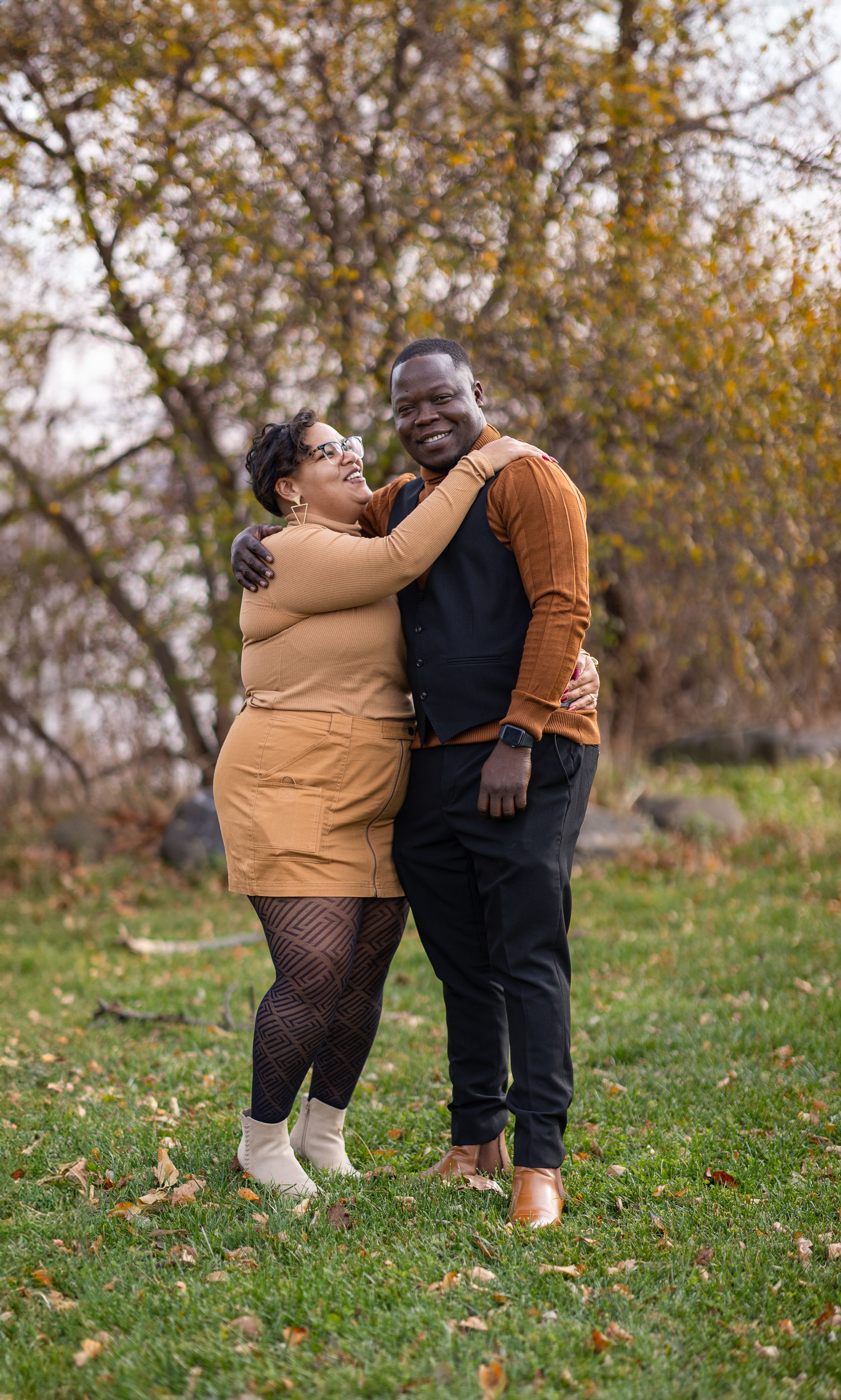 A couple shares joyful moments together in a fall outdoor setting with autumn leaves on the ground.