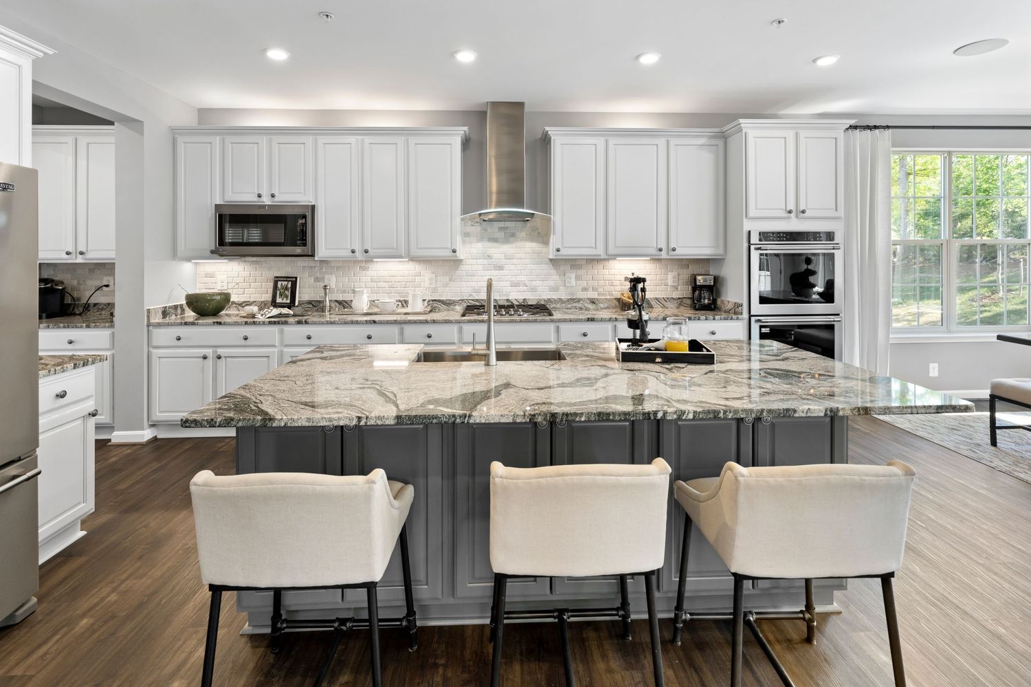 Contemporary kitchen with white cabinets, gray island and upholstered bar stools features modern pendant lighting.