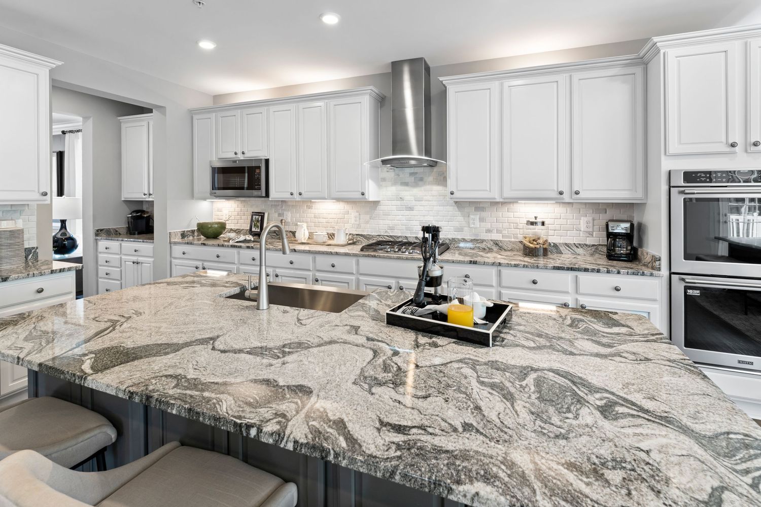 Modern kitchen featuring dramatic marble-patterned countertops, white cabinets and stainless steel appliances.