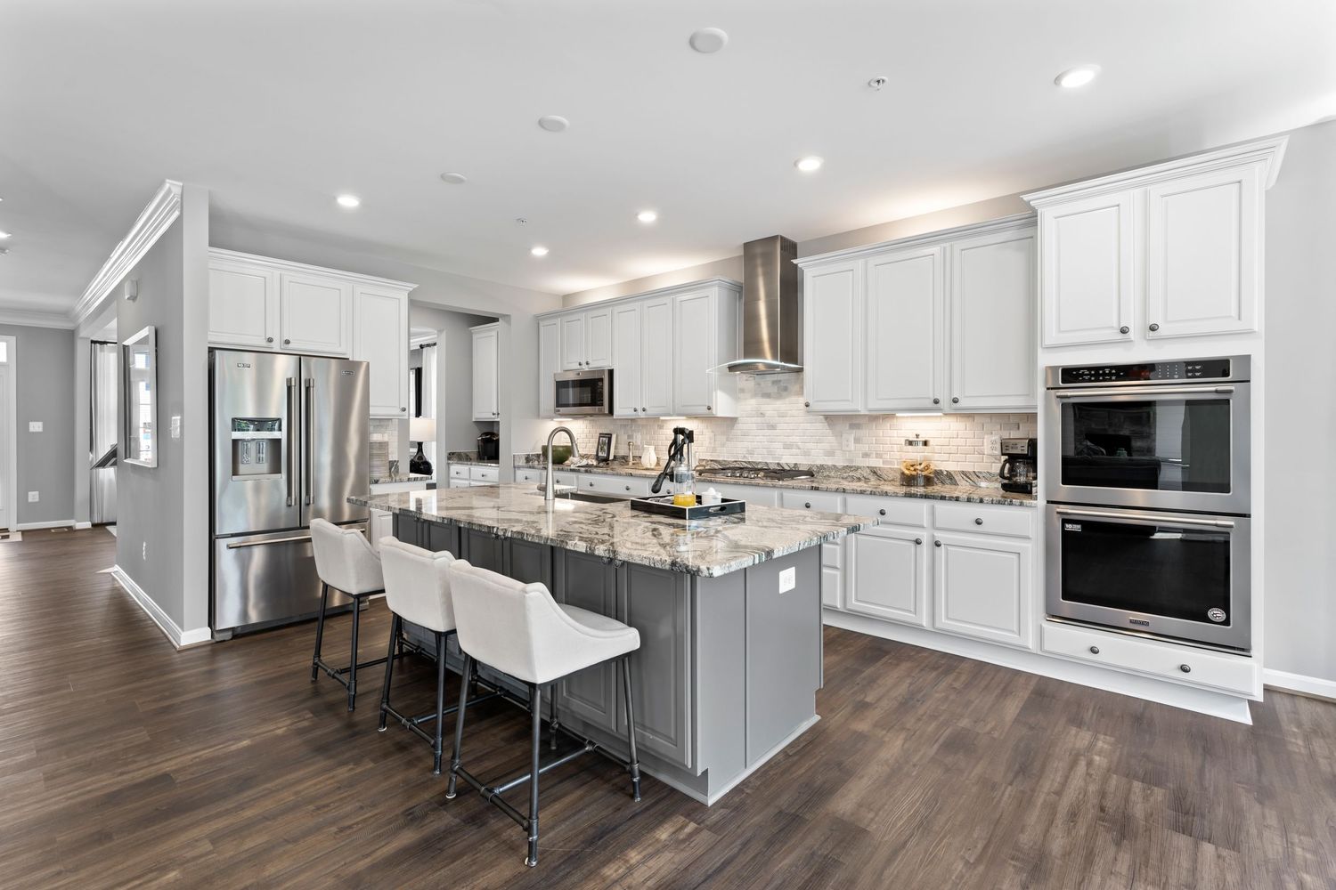 Upscale white kitchen with stainless steel appliances, granite countertops and center island with seating.