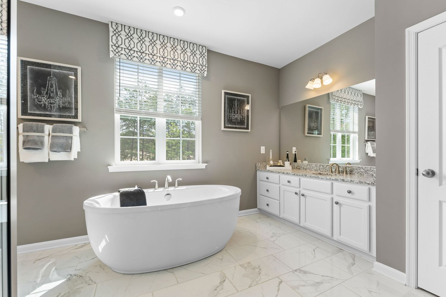Modern white and gray master bathroom featuring marble countertops, freestanding tub, and elegant lighting fixtures.