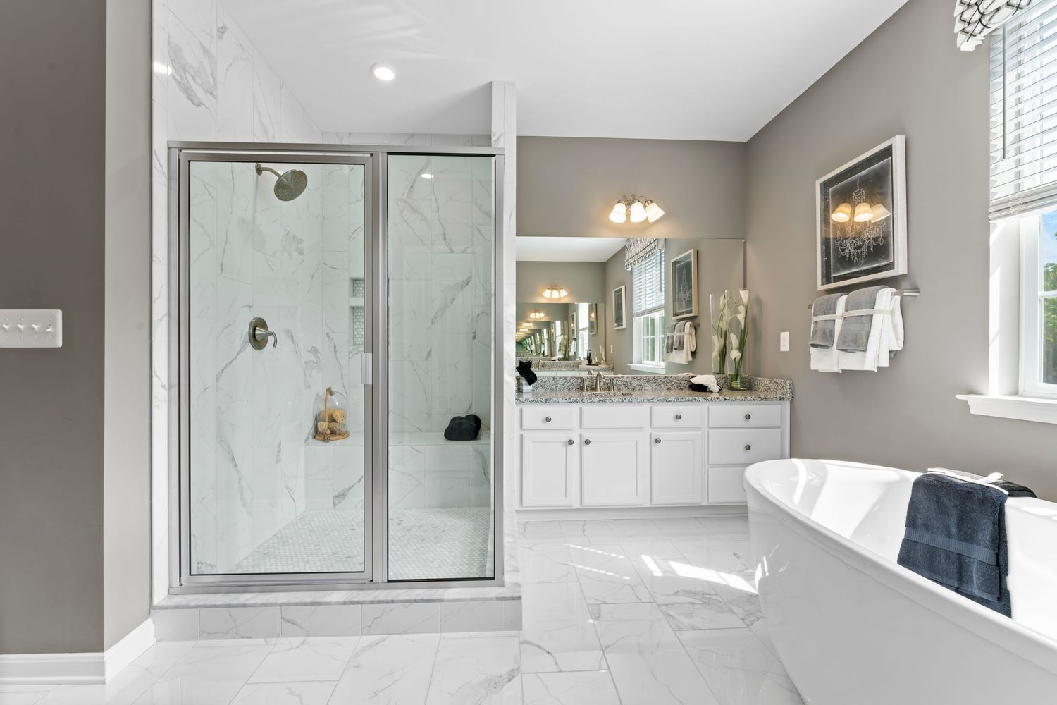 Luxurious bathroom interior with white vanity, marble countertops and glass shower enclosure.