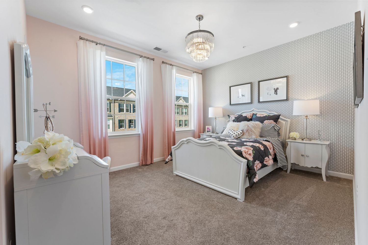 Serene bedroom with pink curtains, striped wallpaper and crystal chandelier showcases elegant white furniture.