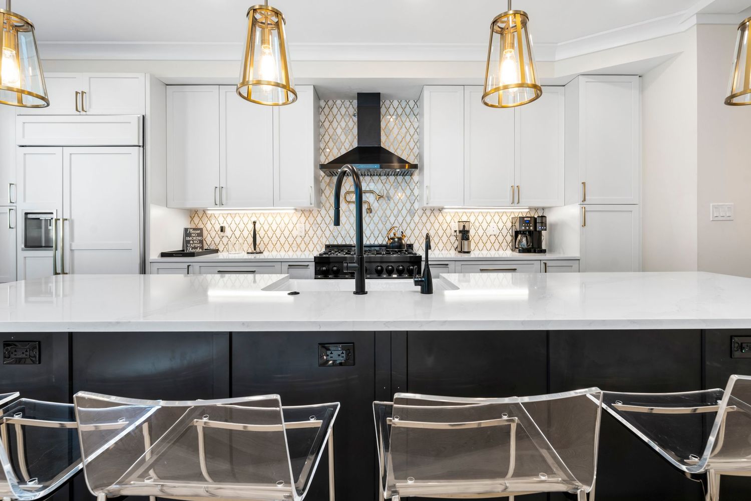 Modern kitchen with black and white contrast featuring gold pendant lights and acrylic bar stools.