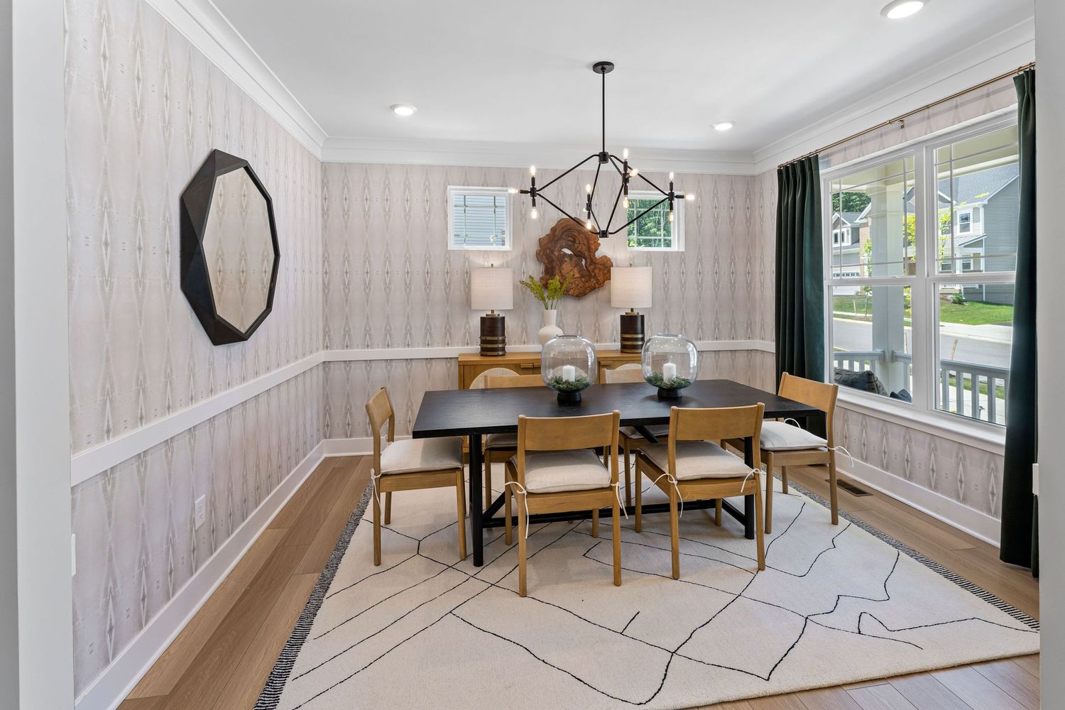 Elegant dining room with geometric area rug, modern chandelier and teal curtains showcases a round wooden table.
