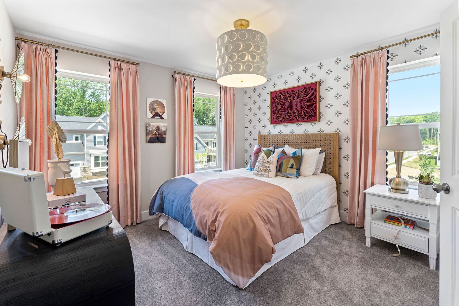 Bright bedroom with floral wallpaper, pink curtains and natural light from multiple windows.