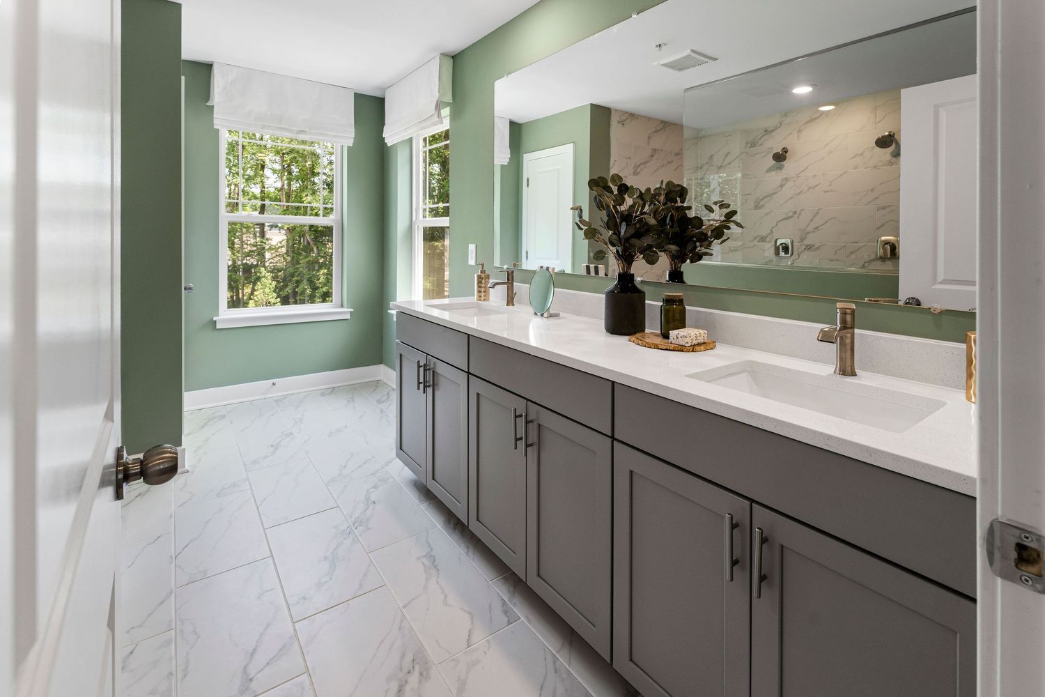 Luxurious bathroom with mint green walls features a long gray vanity, double sinks and marble-look tile flooring.