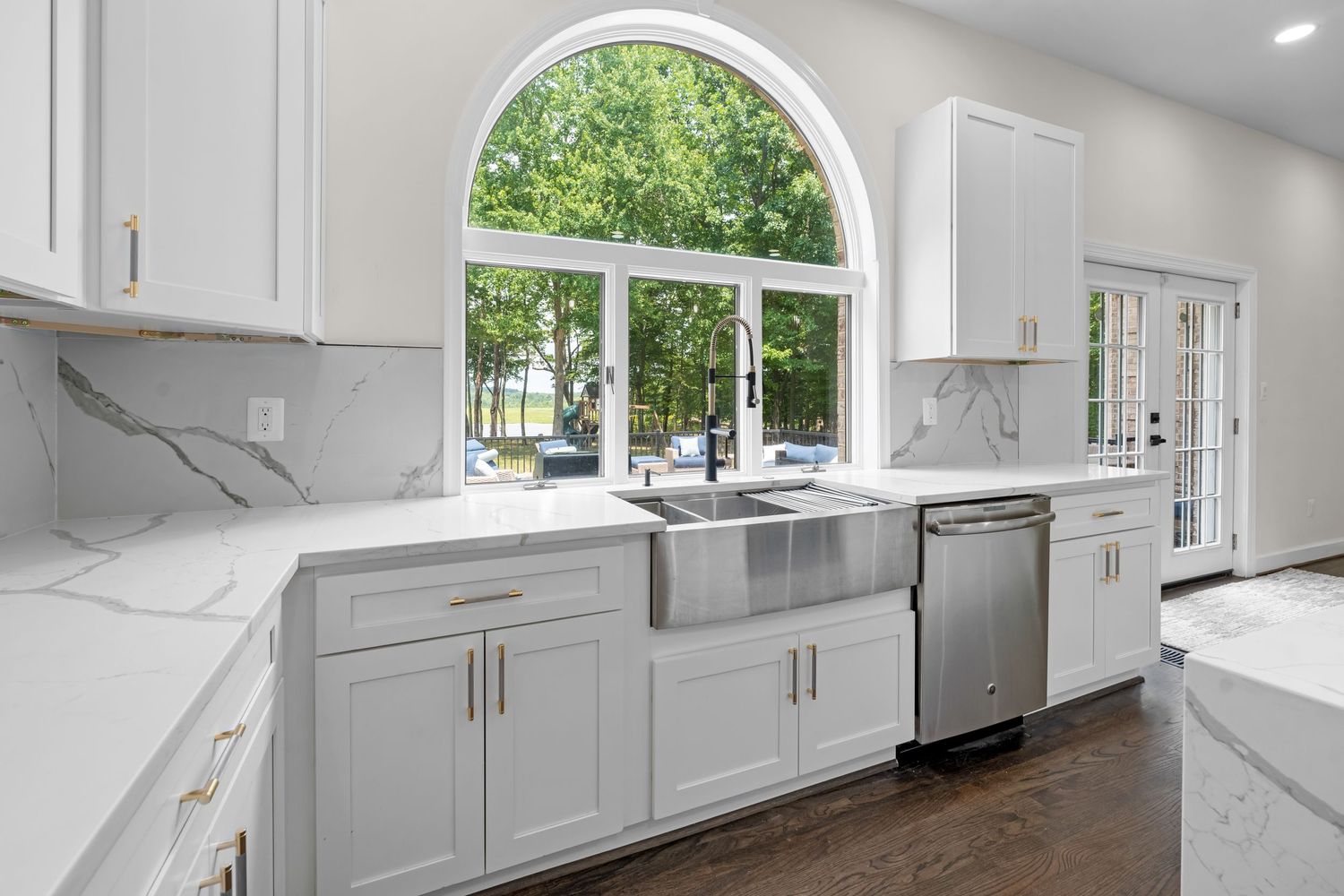 Bright white kitchen with arched window, marble backsplash, and stainless steel appliances.