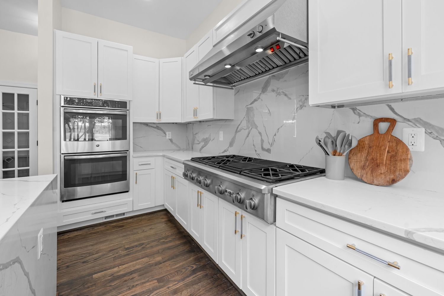 Modern white kitchen with marble backsplash, gas range, and wall ovens.
