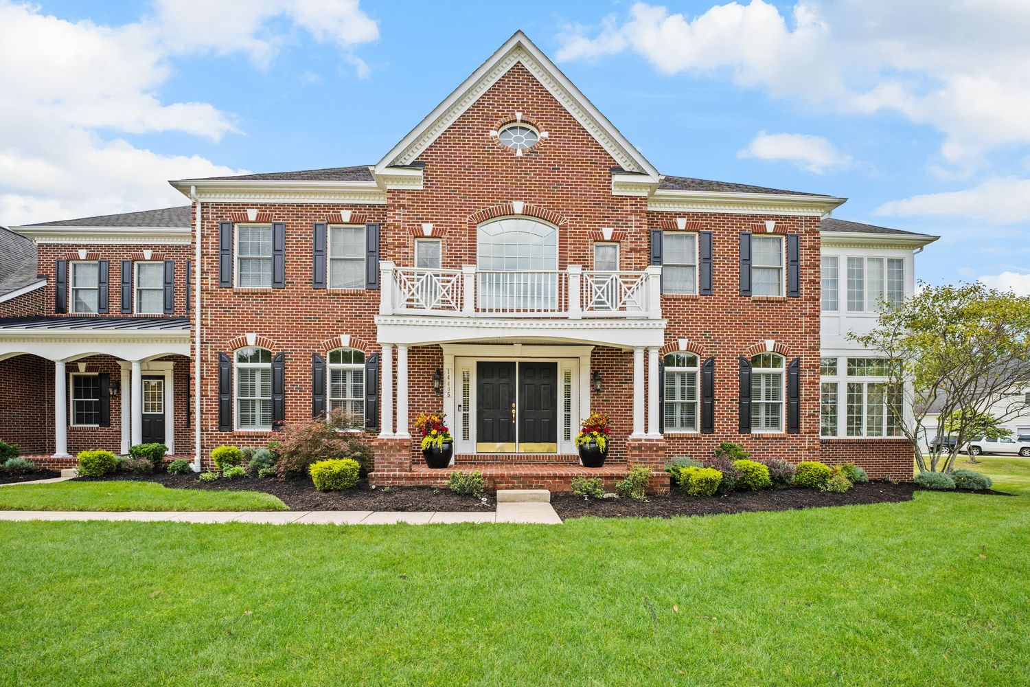 Elegant brick mansion with white columns, balcony, and manicured front lawn.