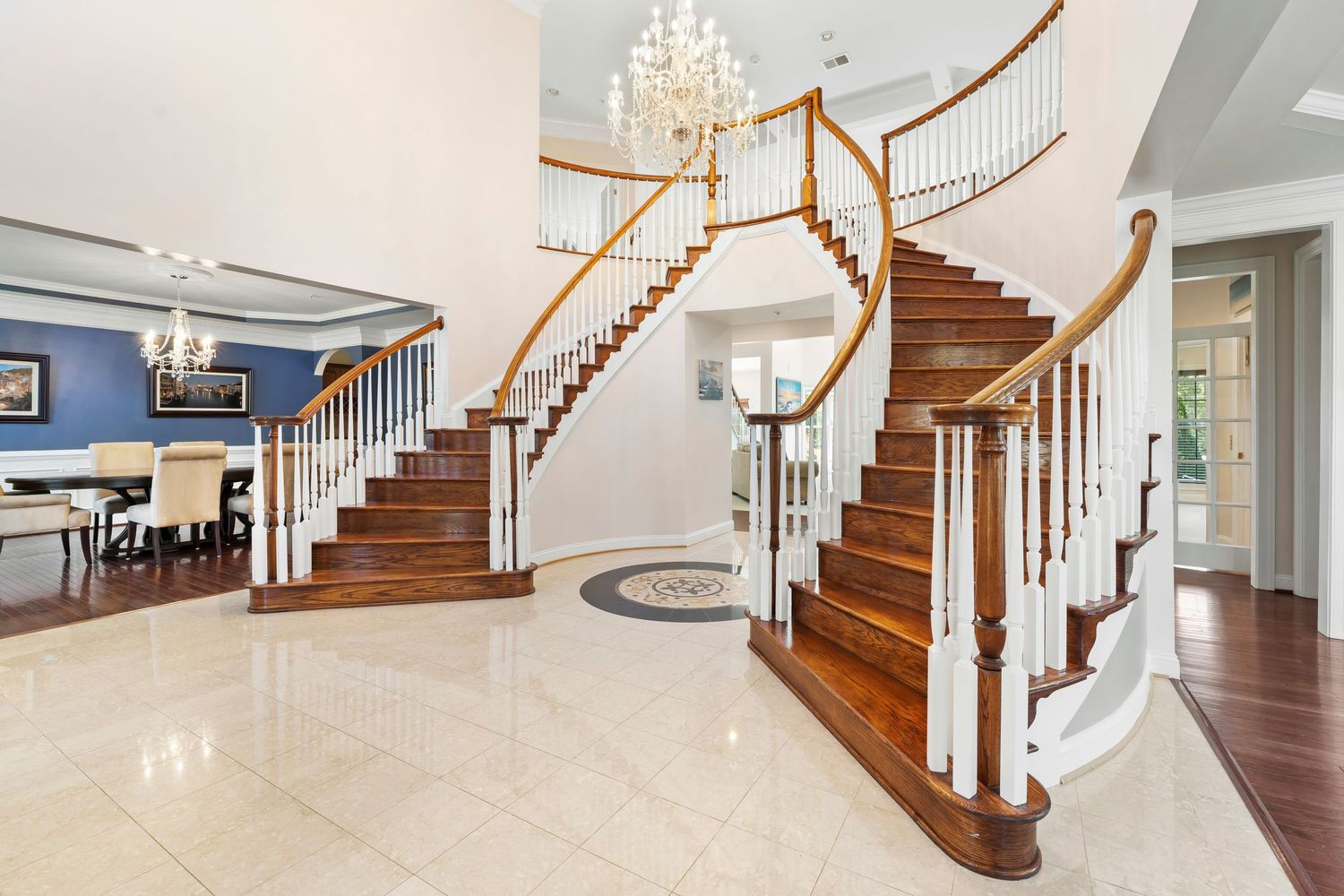 Curved wooden staircase with white spindles and elegant chandelier creates dramatic entryway.