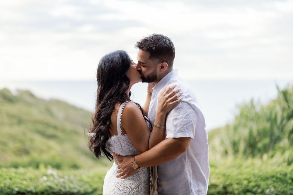 A couple embracing on a grassy hillside with a scenic view in the background.