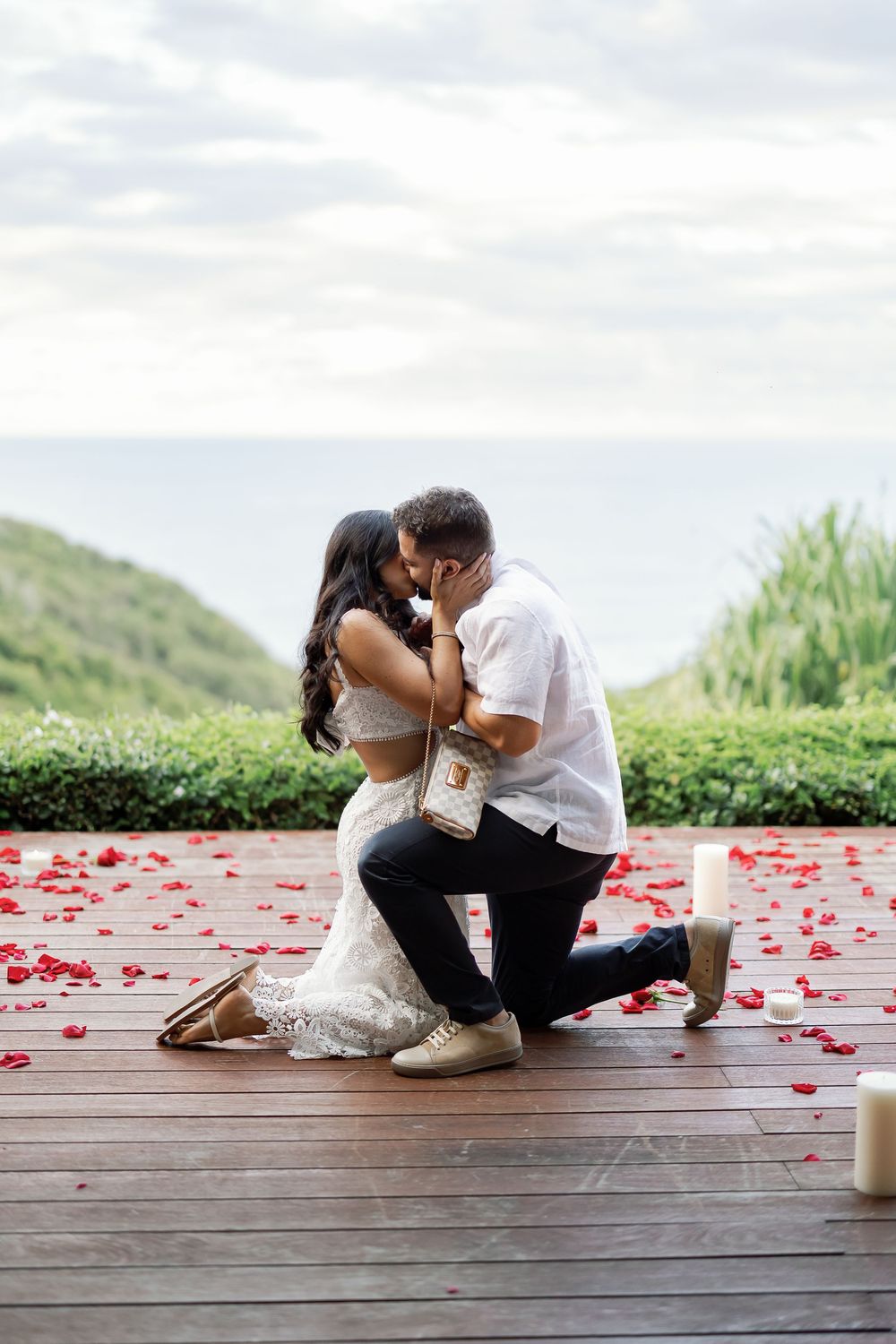 A couple embracing and kissing on a wooden deck with rose petals scattered around them.