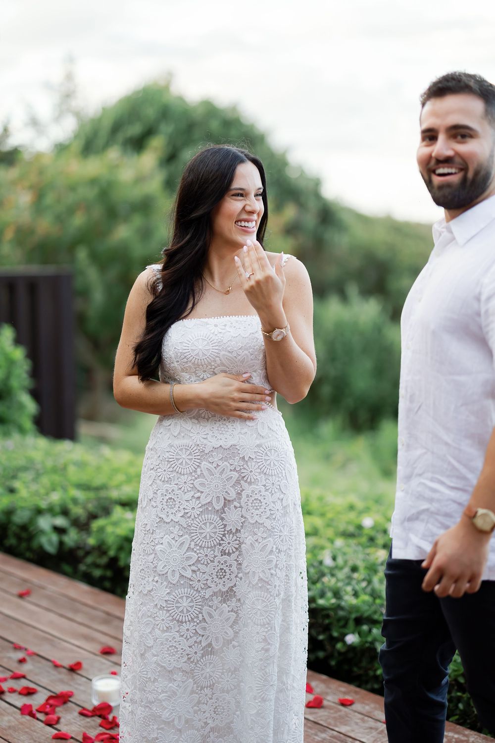 A couple standing together in a garden setting, with the woman smiling and the man embracing her.