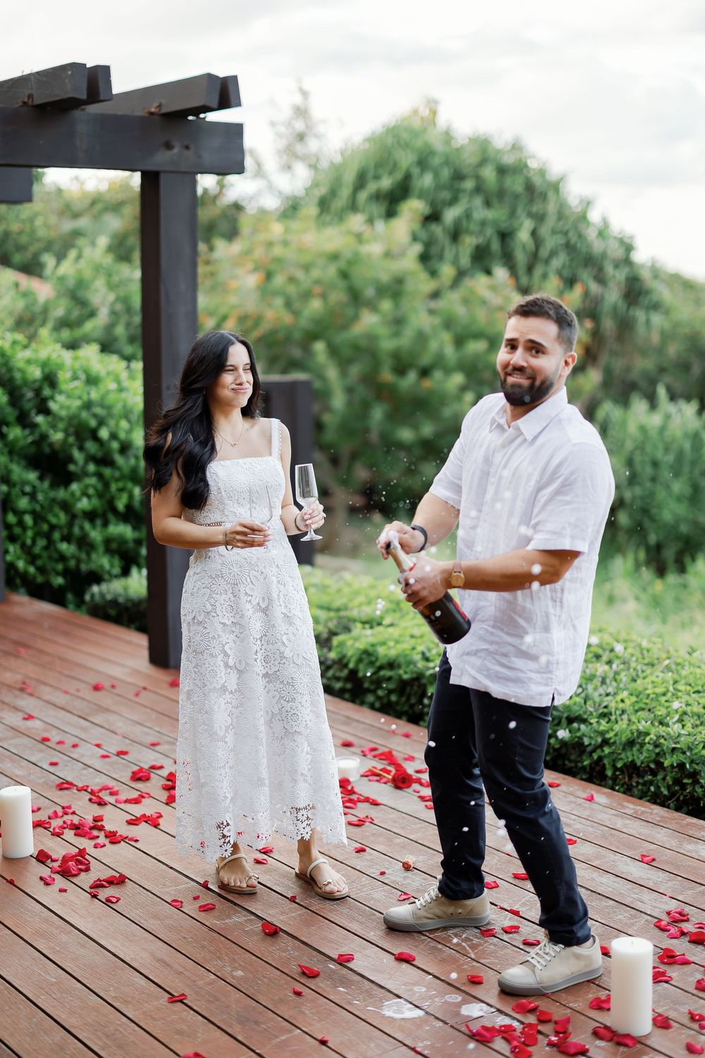 A couple standing on a wooden deck, with the woman holding a glass of wine and the man standing next to her.