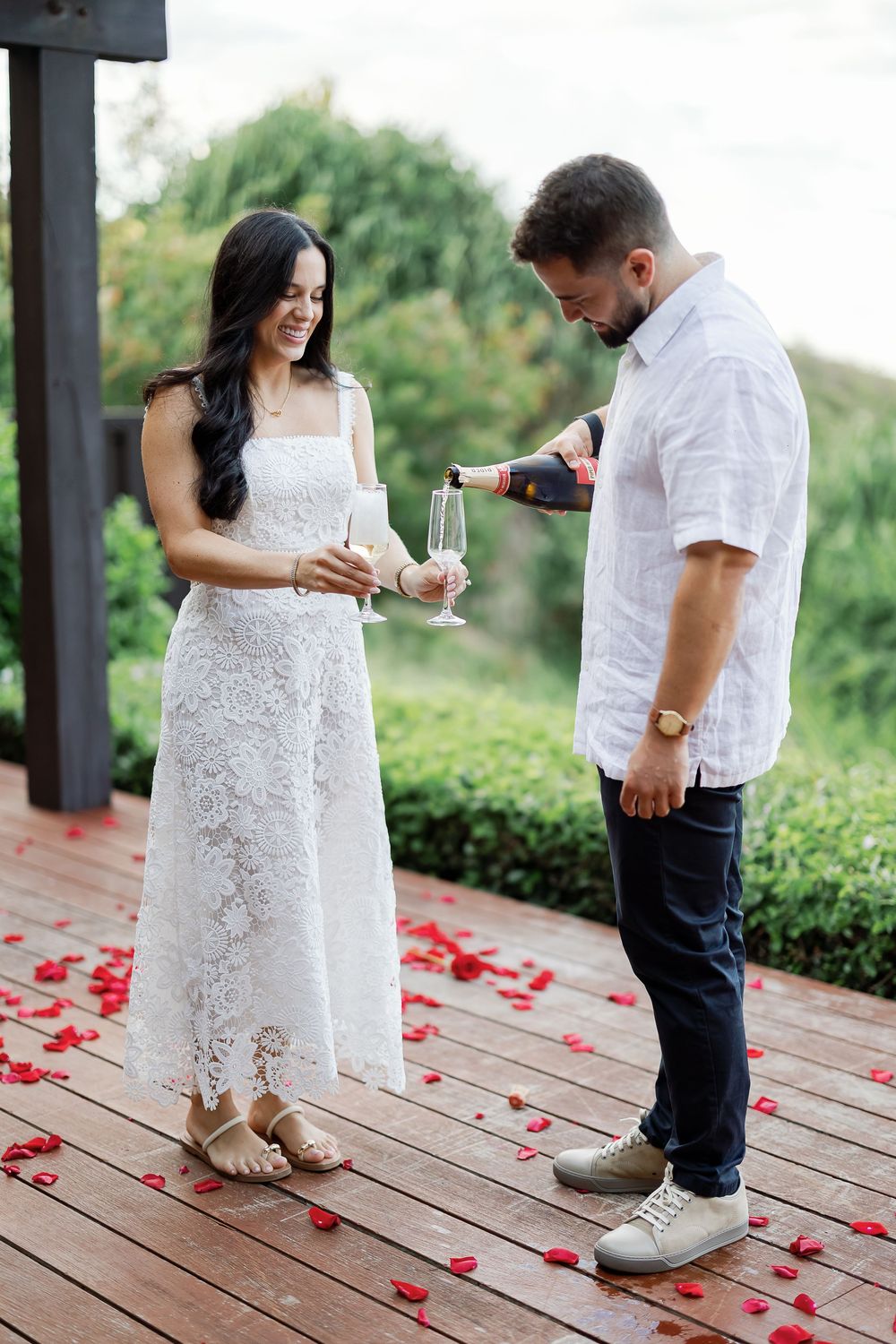 A couple standing on a wooden deck, with the woman holding a glass of wine and the man standing next to her.