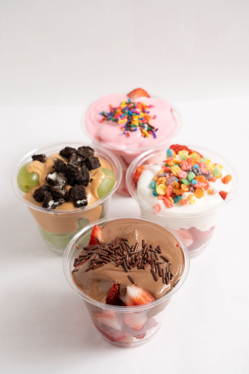 Colorful dessert cups filled with different flavored puddings and toppings like sprinkles, cookies, and fruit.