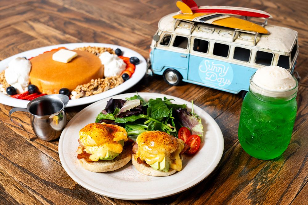 Brunch setup with eggs benedict and pancakes alongside a vintage blue VW bus toy and green drink.
