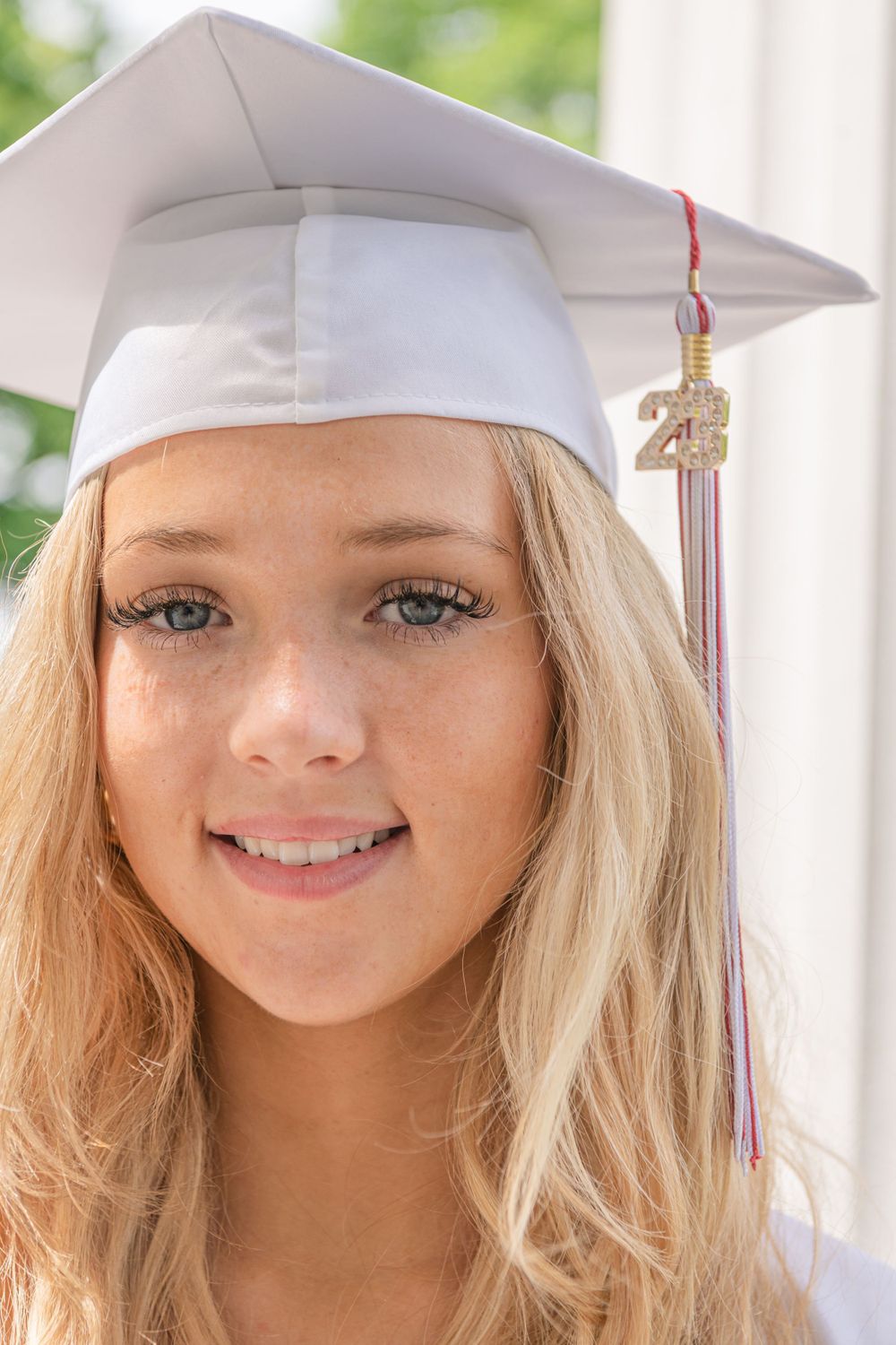 Close-up portrait of graduate in white cap with tassel against column background.
