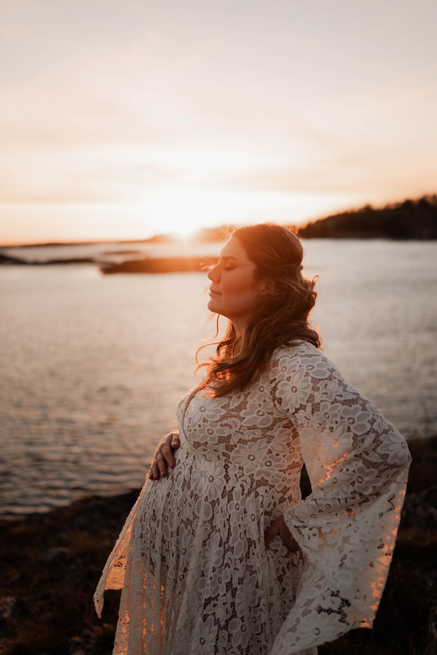 Gravid kvinna i solnedgången på klippor med bohemisk klänning
