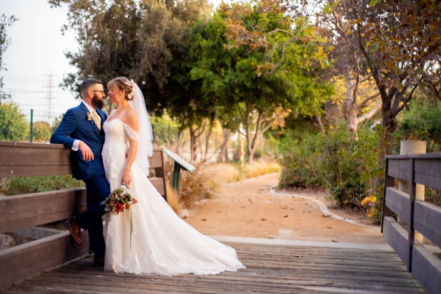 Outdoor wedding photography in Orange County featuring a bride and groom standing together on a wooden bridge during a couple’s portrait ses