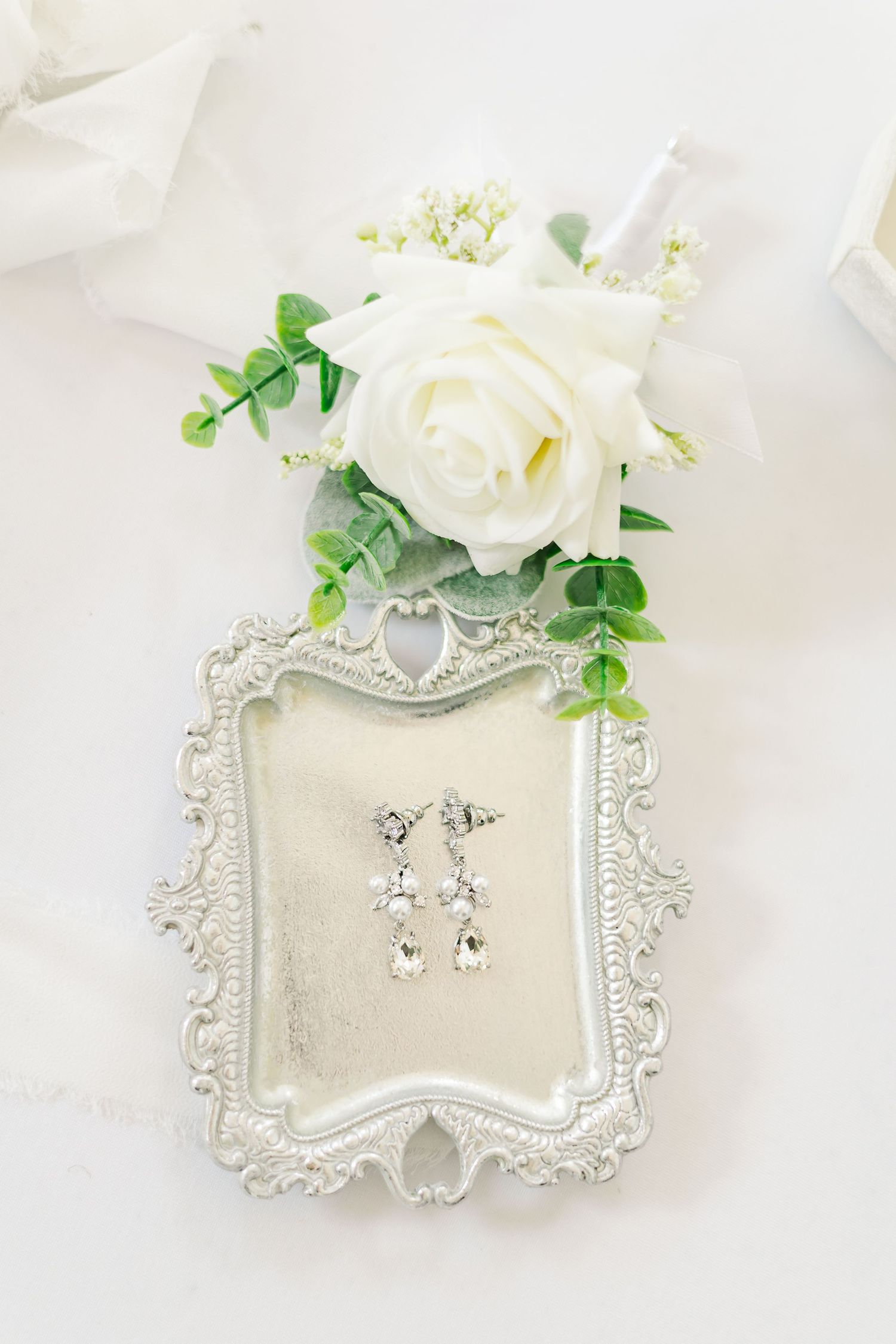 Elegant silver jewelry display trays with white roses and greenery on light background.