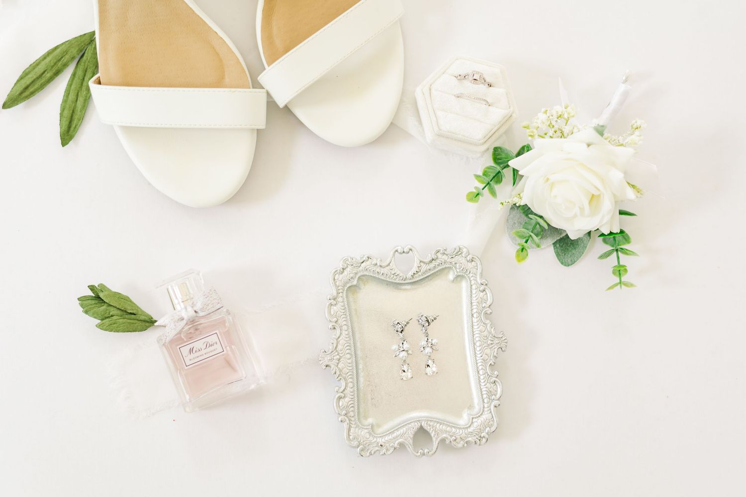 Delicate bridal accessories and jewelry styled with white flowers on light background.