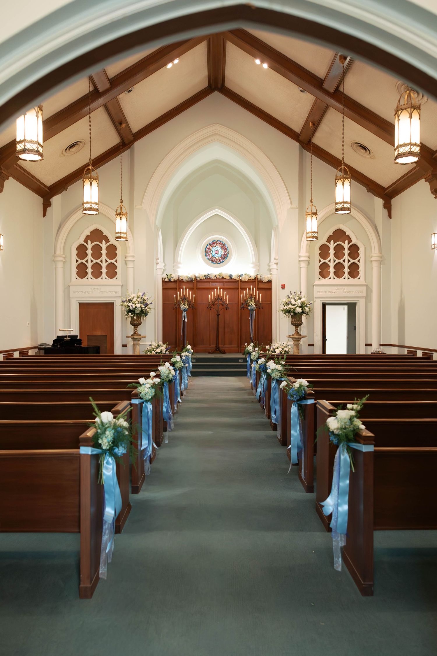 Elegant church interior with wooden pews adorned with blue ribbon and white floral arrangements leading to altar.
