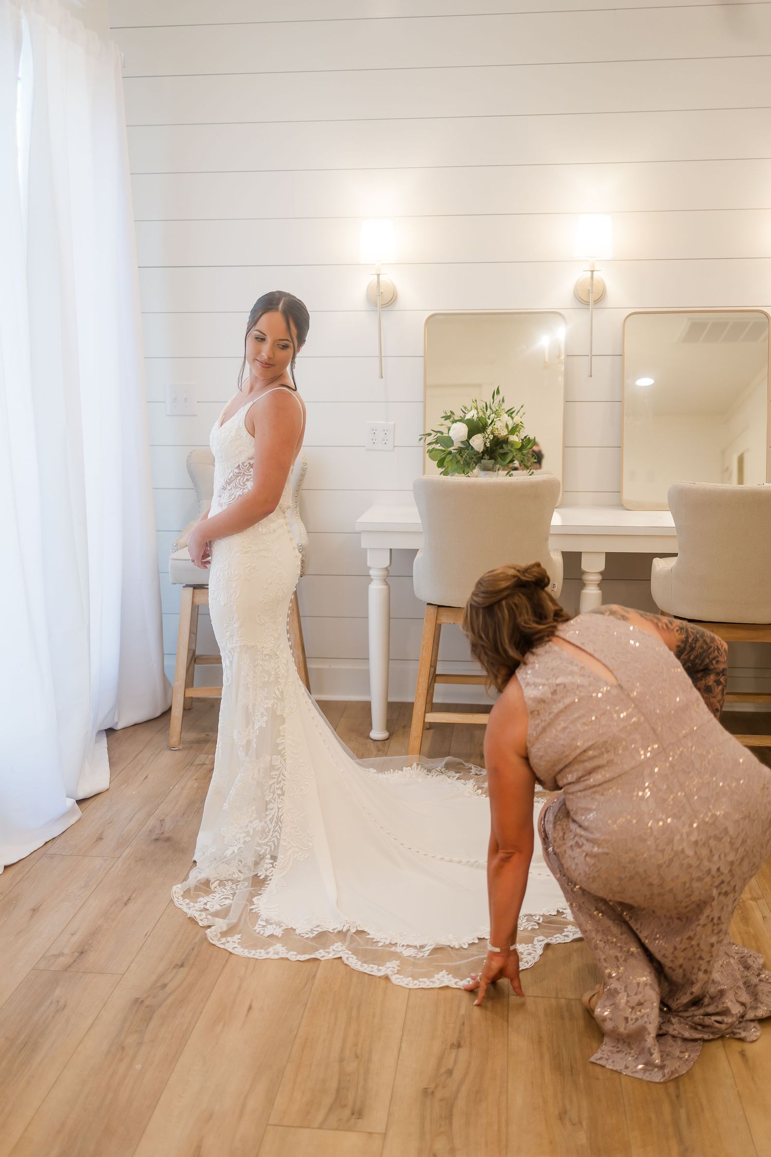 Wedding dress fitting session showing lace train details on light wooden floor.