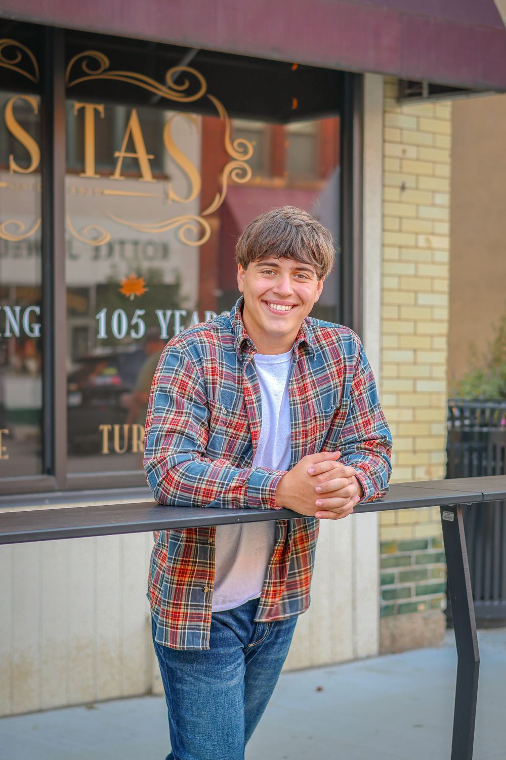A casual portrait outside a vintage storefront with a plaid flannel shirt leaning against a railing.