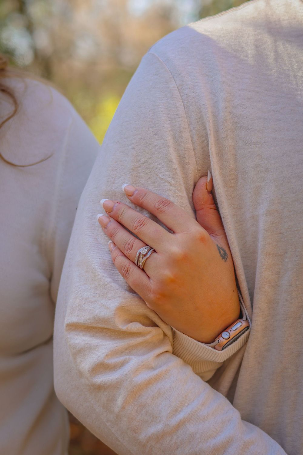 Close-up of hands with wedding rings embracing in a tender moment against a cream colored sweater.