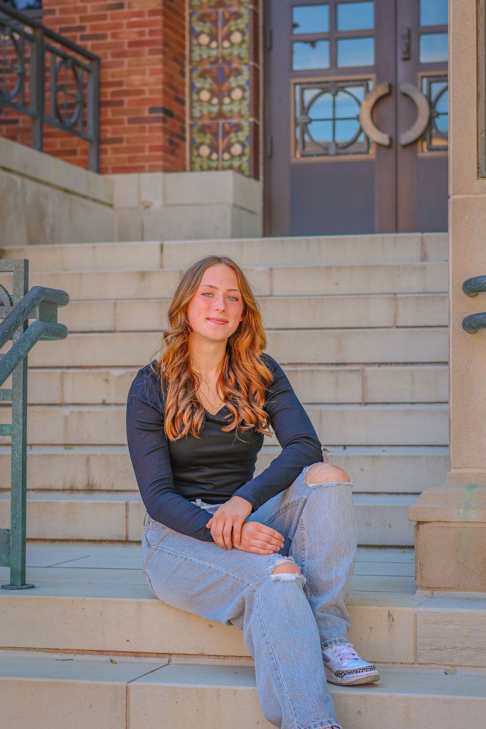 Portrait on concrete steps outside a brick building with decorative doors.